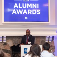 Quincy Williams speaking in microphone with 2024 Alumni Awards sign behind him